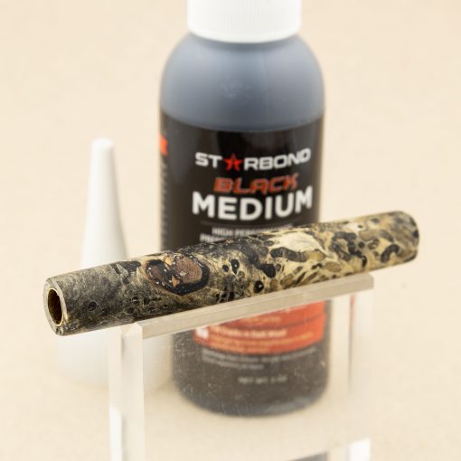 A bottle of black CA glue with a finished burl pen barrel on a display stand