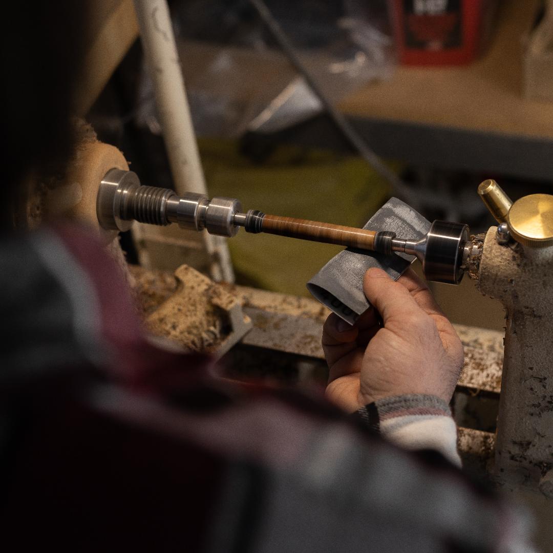 A penturner sanding a maple burl pen blank that is turning on a lathe with micro mesh sheets after applying Starbond Black CA Glue