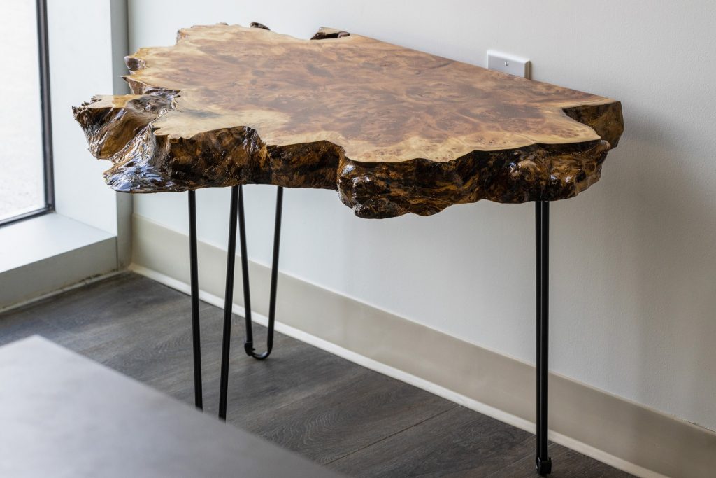 slab of live edge cottonwood burl turned into a resin epoxy side table with three legs, pictured standing up against a wall with live edge facing out.