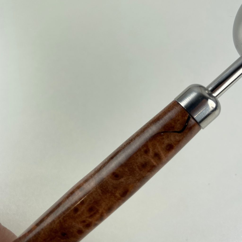 Close up of a crack in a redwood lace burl pen blank, assembled onto a measuring spoon kit, from William Wood-Write Ltd filled with dark brown starbond CA glue.