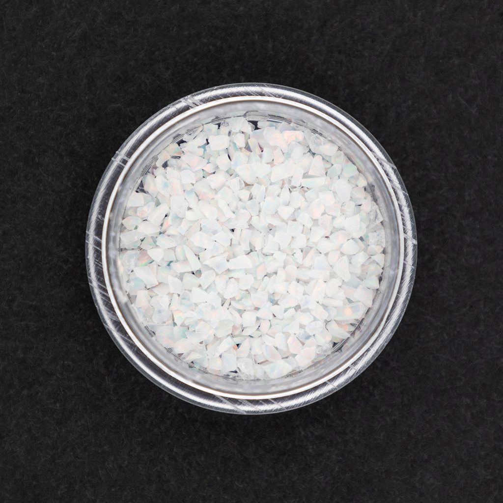 1 gram container of synthetic opal inlay material in fire and snow from William Wood-Write Ltd. against black background.
