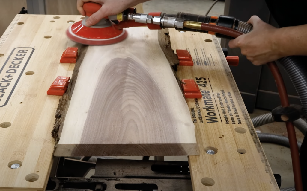 Live edge black walnut charcuterie board from William Wood-Write Ltd. being sanded with a handheld sander.