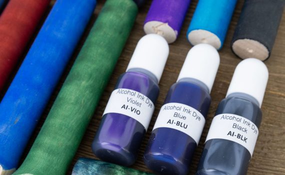 pen blanks dyed bright colours beside three small bottles of alcohol ink