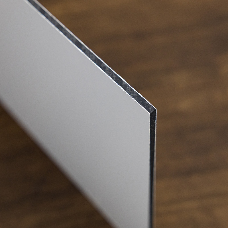 A closeup of a flat rectangular piece of aluminum composite panel with white sides and a black center.