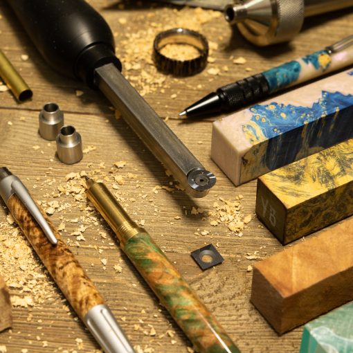 A chisel, pens, wooden pen blanks, bushings and rings made on a lathe laid out on a wooden table.