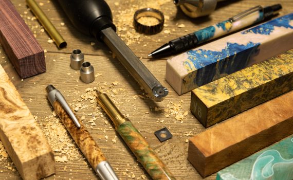 A chisel, pens, wooden pen blanks, bushings and rings made on a lathe laid out on a wooden table.