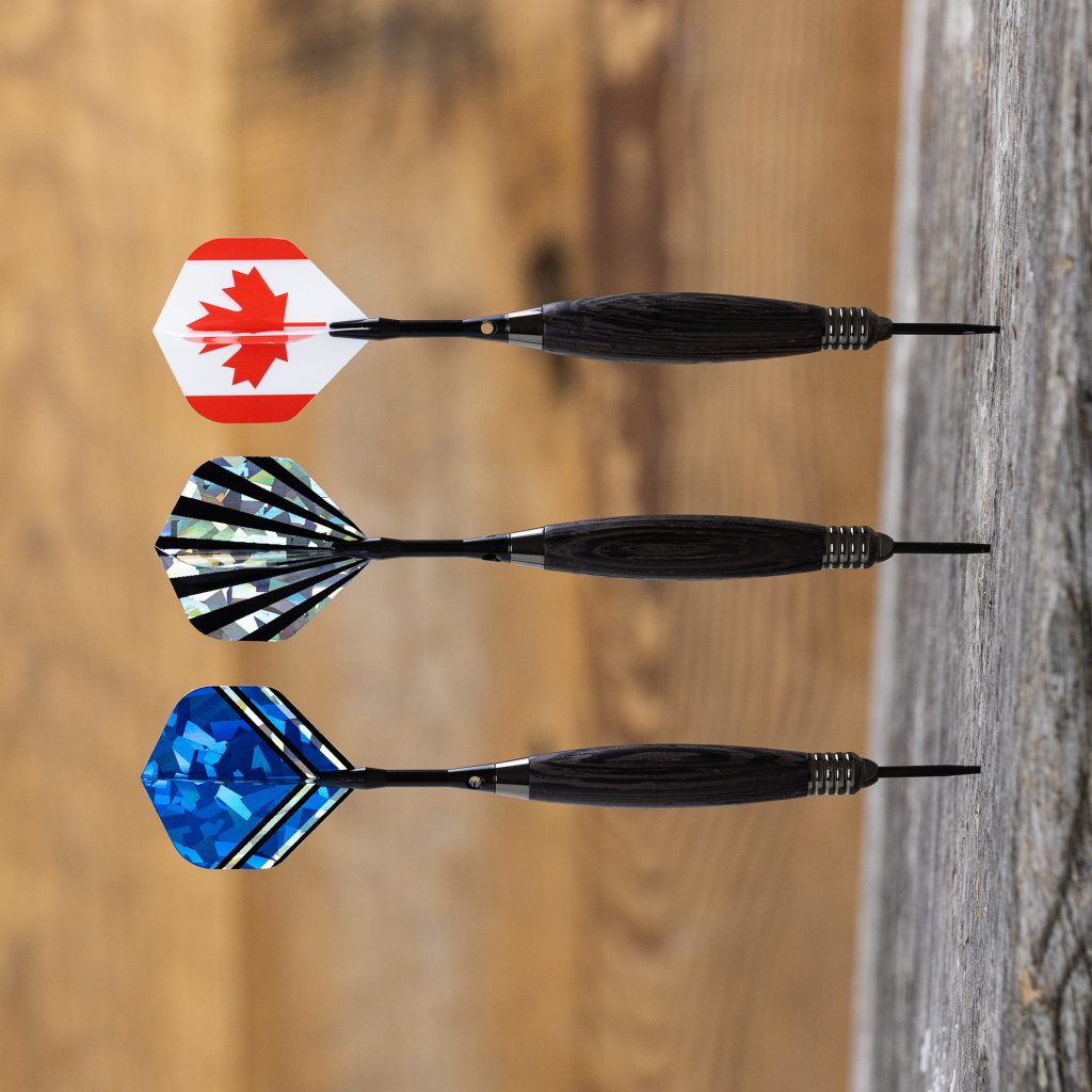 Three darts stuck in a piece of wood, each with different flights.