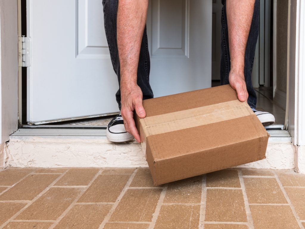 A person bent over picking up a package on a porch.