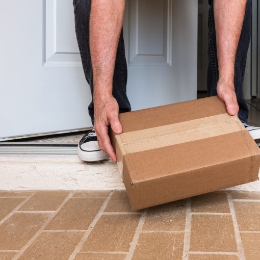 A person bent over picking up a package on a porch.