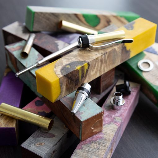 Disassembled parts of a pen turning kit sitting on different coloured acrylic and burl pen blanks