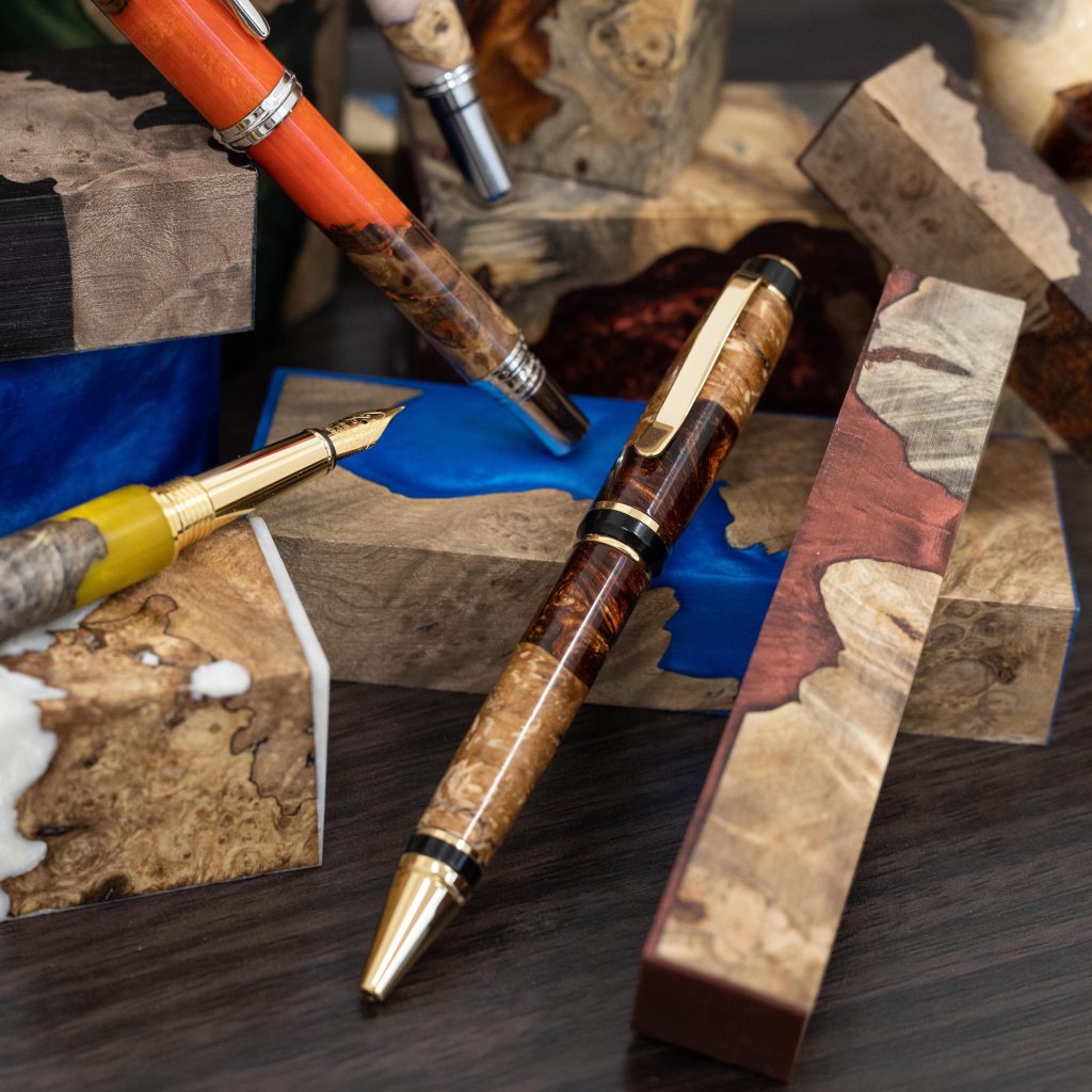 Three colourful handmade pens sitting on a pile of various resin pen blanks