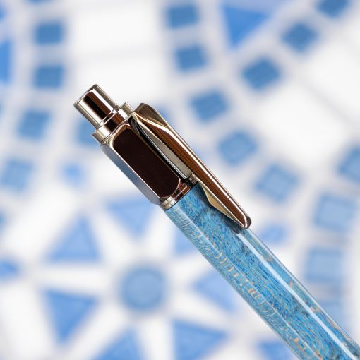 A close-up of a blue pen with gun metal plated click mechanism