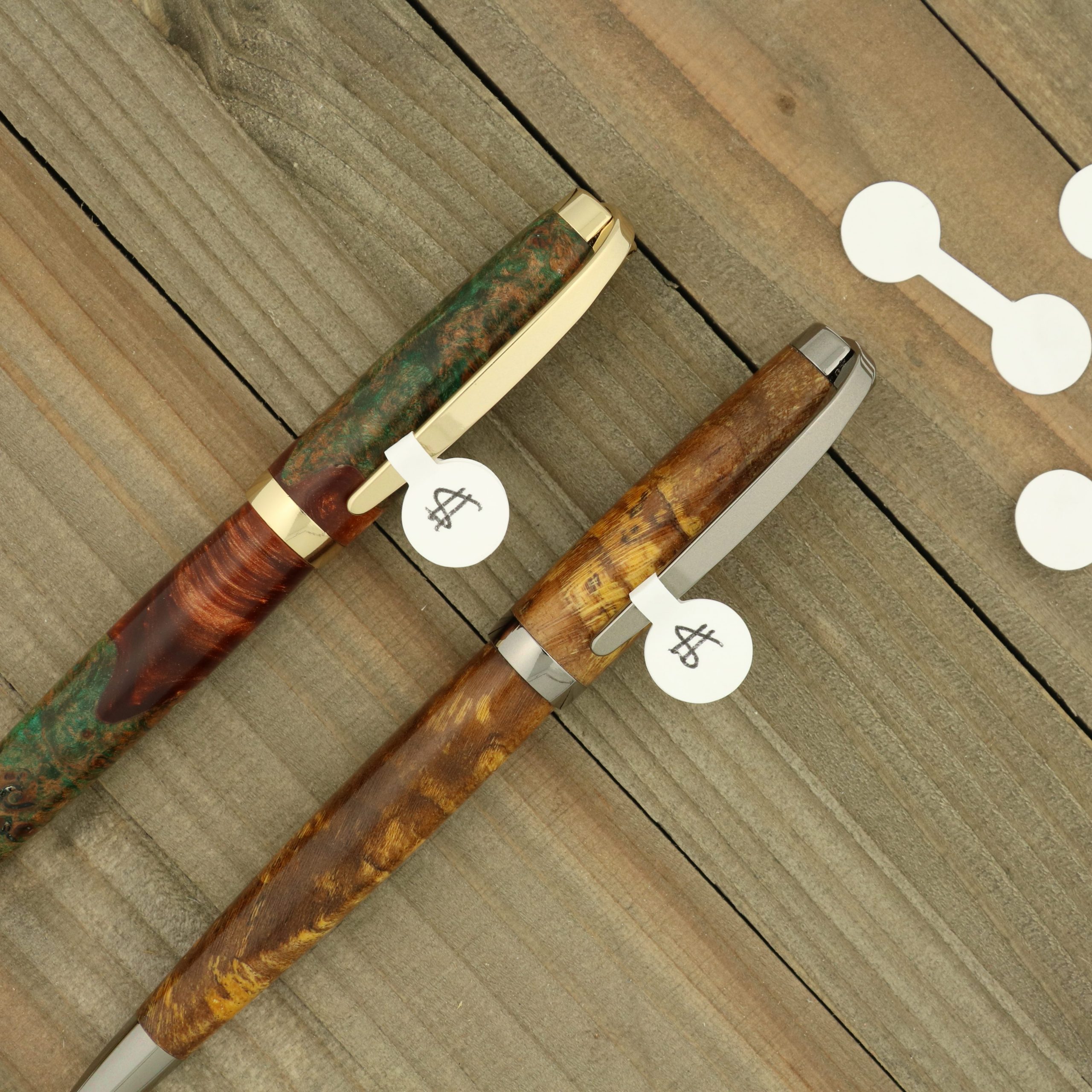 Two wood turned pens laying on weathered wood with price tags showing