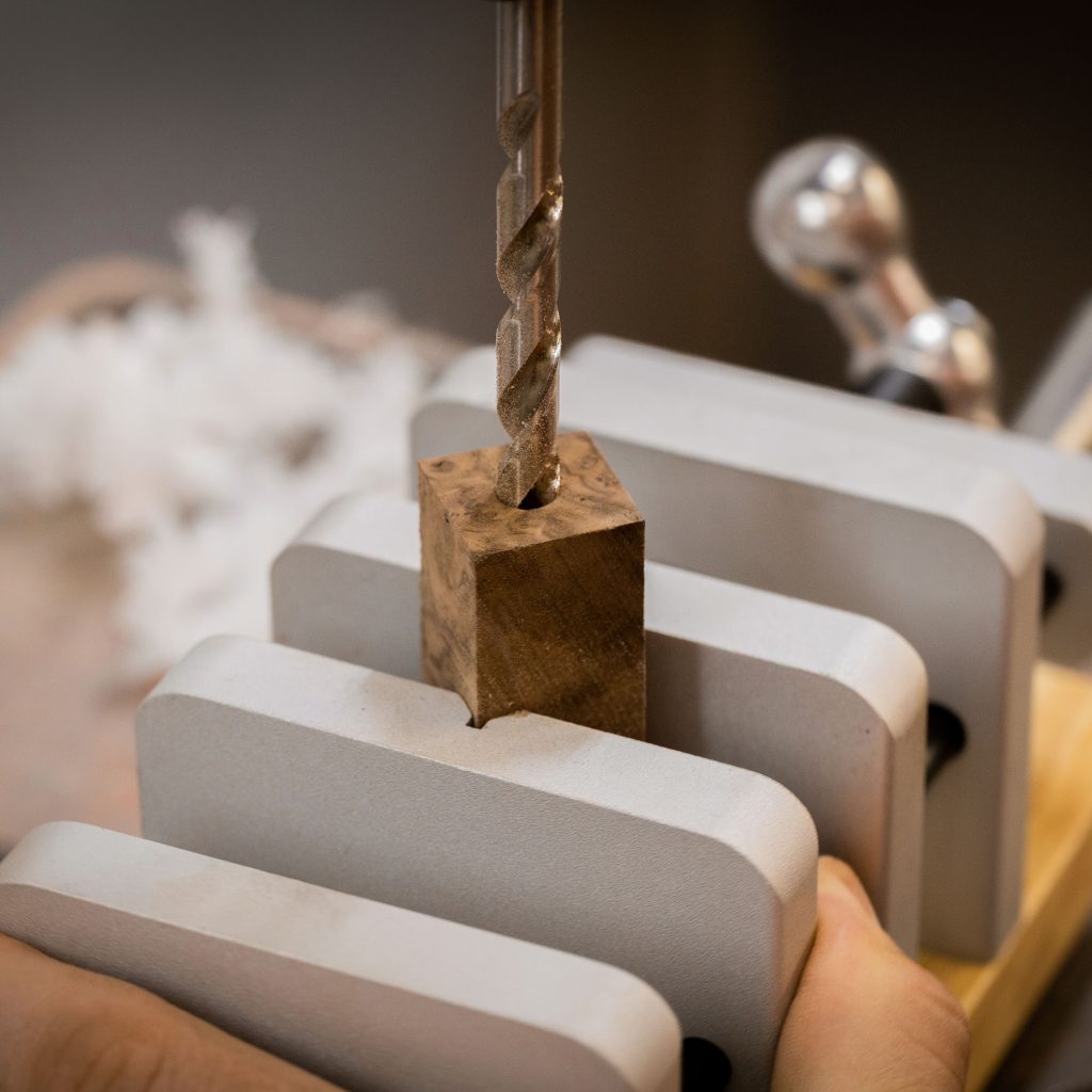 A drill press with a drill bit entering a piece of wood which is held in a centering vise.