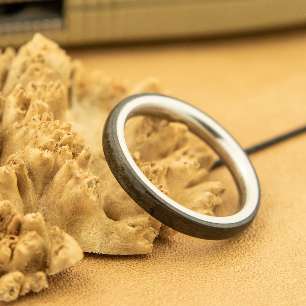 A handmade wooden ring with a metal core displayed on a chunk of burl.