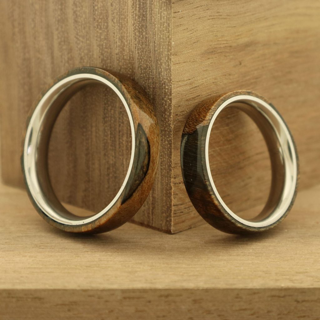 Two handmade wooden rings leaning against a wooden background