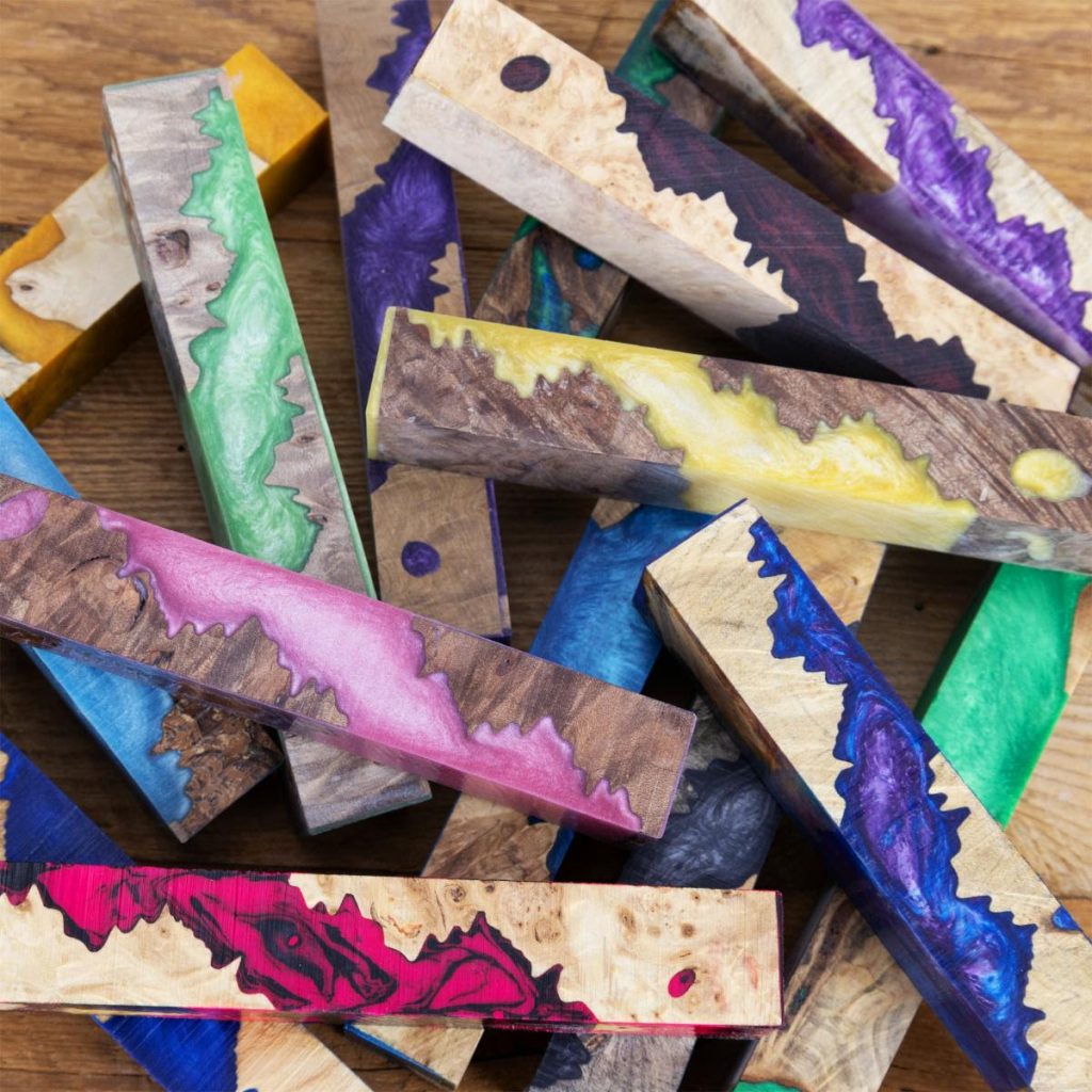 A scattered pile of colourful pen blanks for wood turning made from resin and burl.