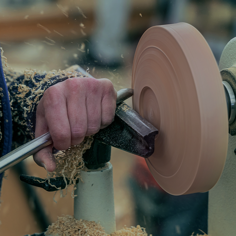 A hand holding a chisel against a round piece of wood that's turning on a lathe