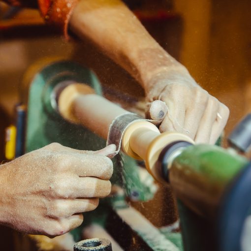 A close up hands sanding a piece of wood on a running lathe