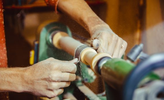 A close up hands sanding a piece of wood on a running lathe