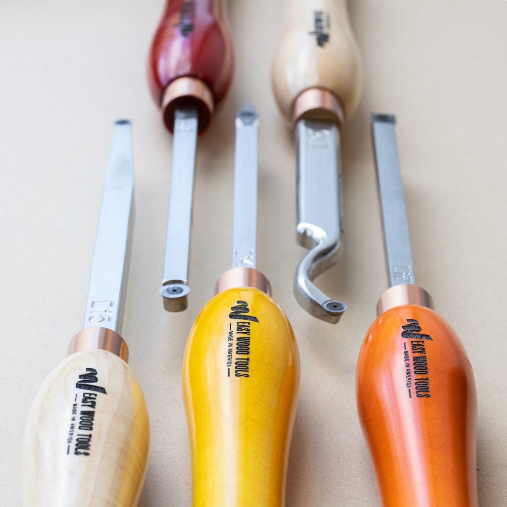 Five different shaped chisels for woodturning are displayed on a neutral background. The handles are orange and yellow wood.