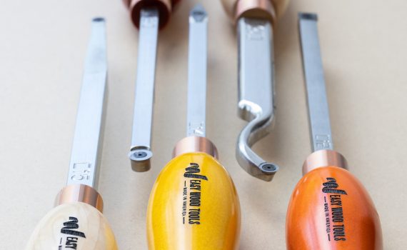 Five different shaped chisels for woodturning are displayed on a neutral background. The handles are orange and yellow wood.