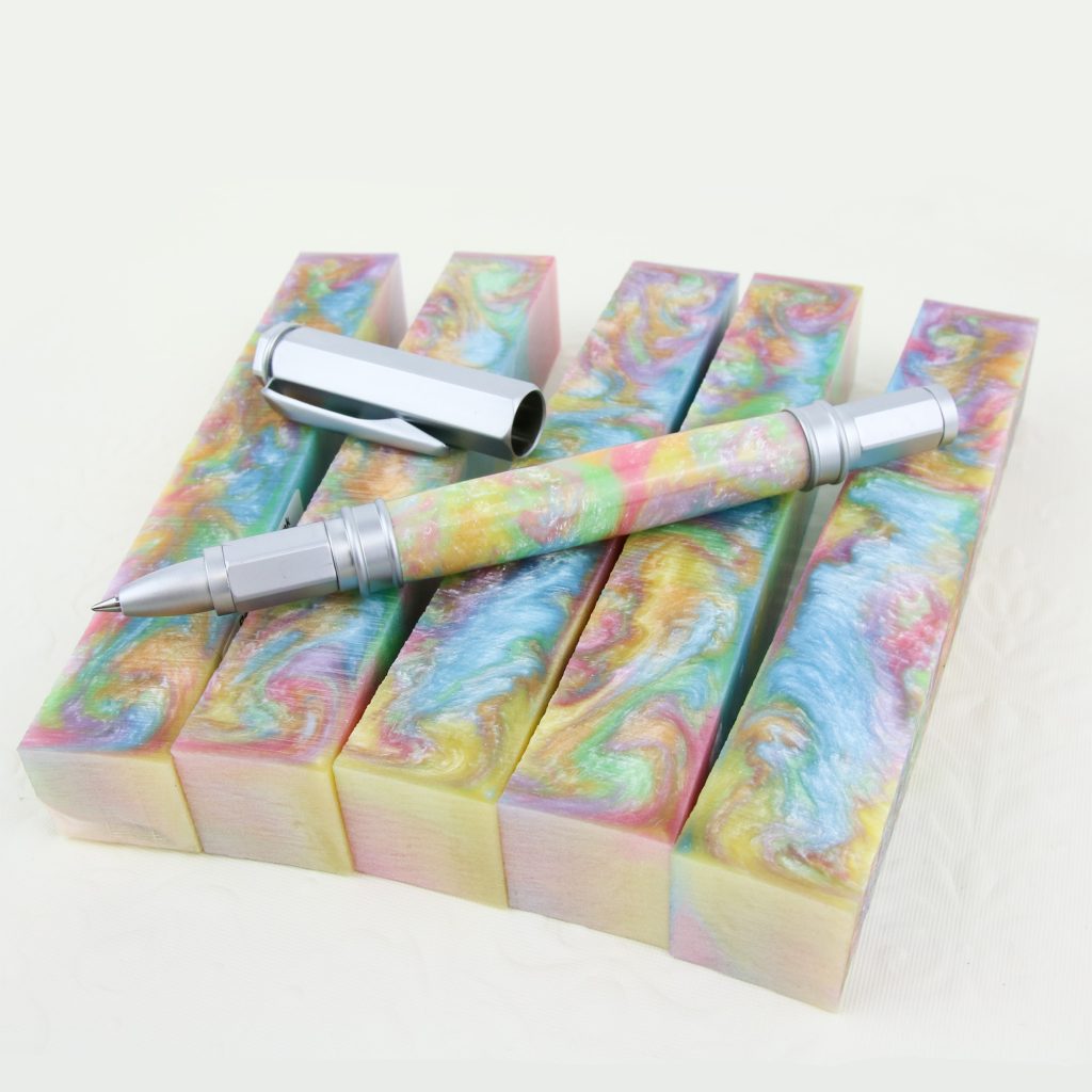 Five multi-coloured pastel pen blanks sit on a white background with a custom handmade pen lying on top.