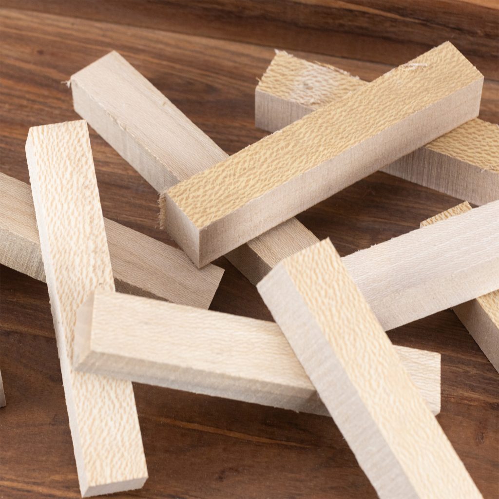 A small pile of sycamore pen blanks in light beige on a dark wood surface