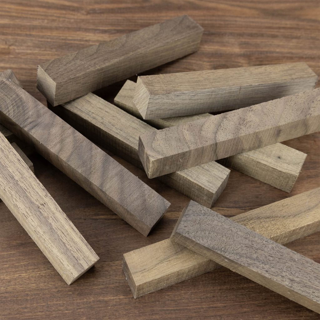 A small pile of dark brown walnut pen blanks scattered on a wooden surface.