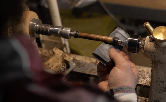 A person sanding a pen blank on a running lathe