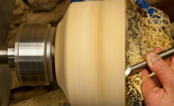 A hand holds a chisel to a wooden bowl that is spinning on a lathe